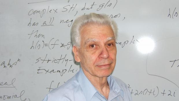 Dante Youla in front of a white board with equations
