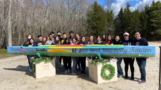 group of students standing behind colorful concrete canoe by lakeside