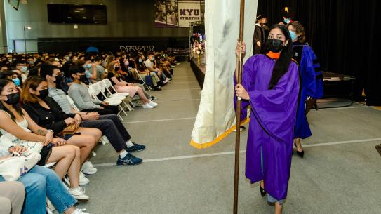 A robed student carries a banner at convocation