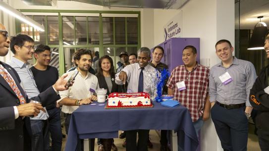 Alumni and members of the Veterans Future Lab look on as Director James Hendon cuts the cake
