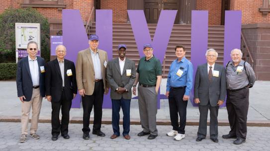 Group of alumni standing in front of oversized purple NYU letters
